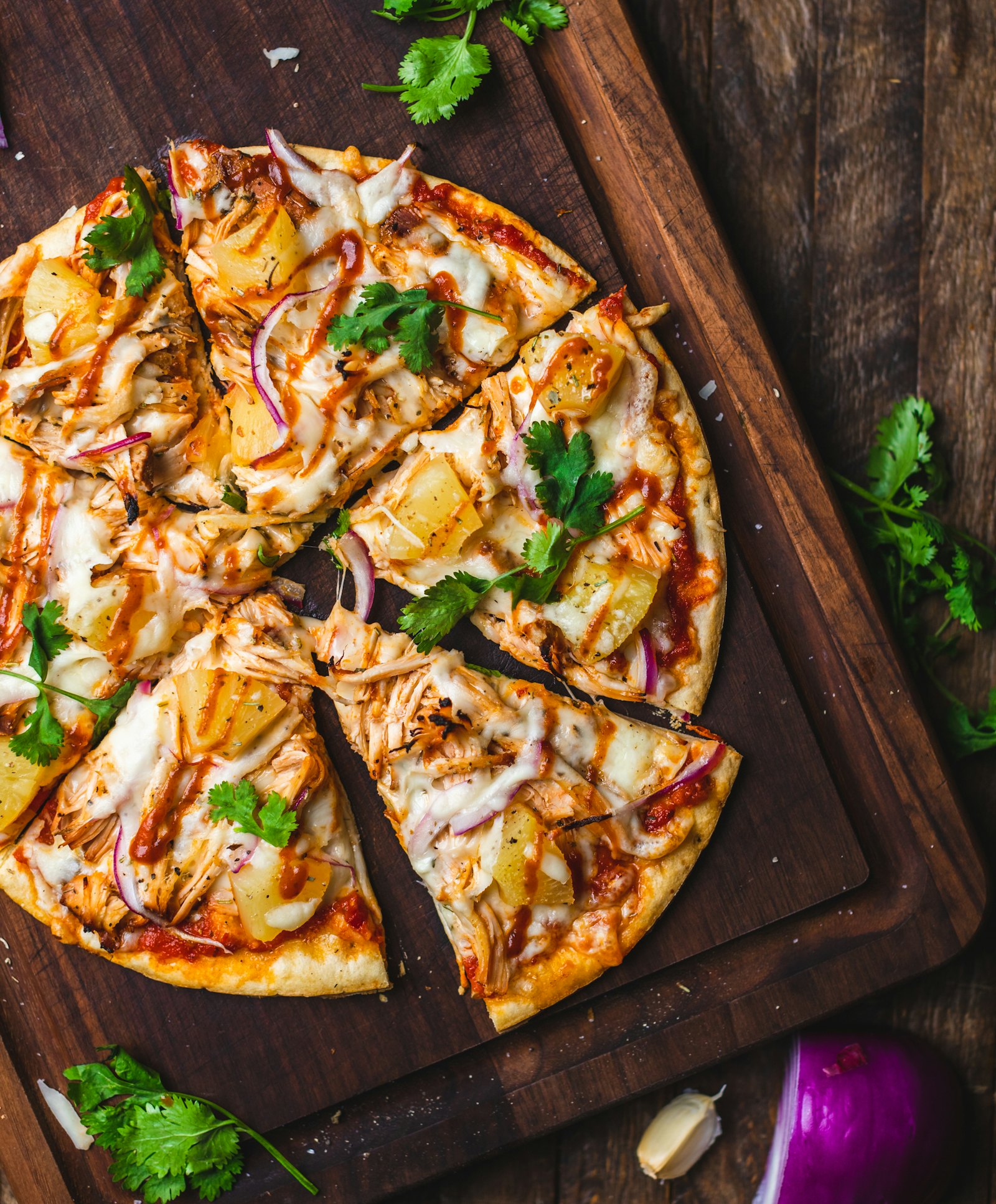 Pizza com frango, cebola roxa e coentro sobre tábua de madeira